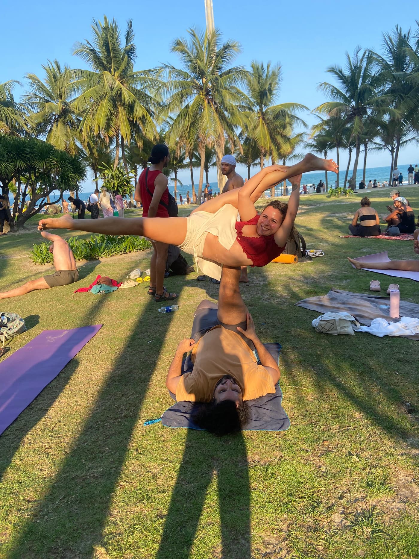 Boyana Vancheva balanced in an acroyoga flying pose on a palm-lined beach at sunset