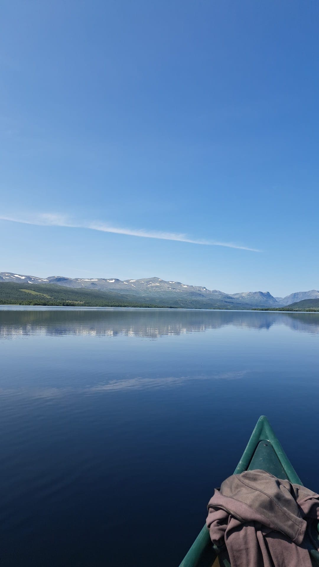 Bow of a green canoe on a glassy Norwegian mountain lake with snow-streaked peaks