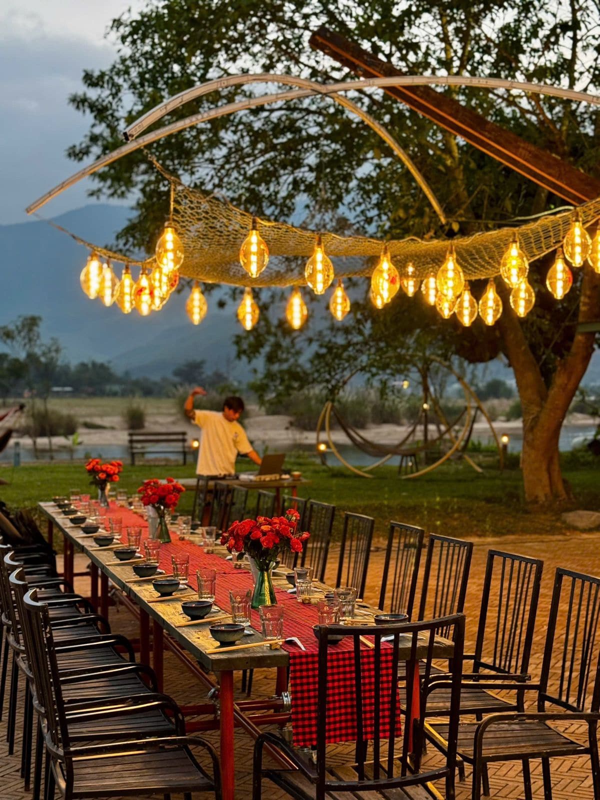 Long communal retreat dinner table set under hanging lanterns at dusk in Thailand