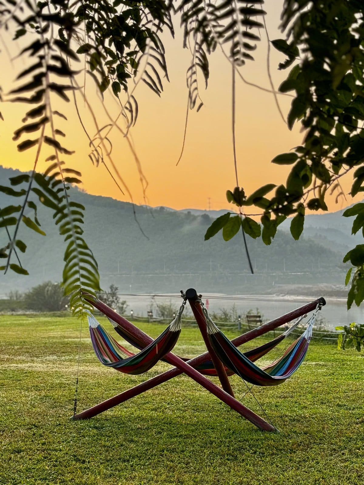 Two woven hammocks on a lawn against an orange sunset over Thai mountains