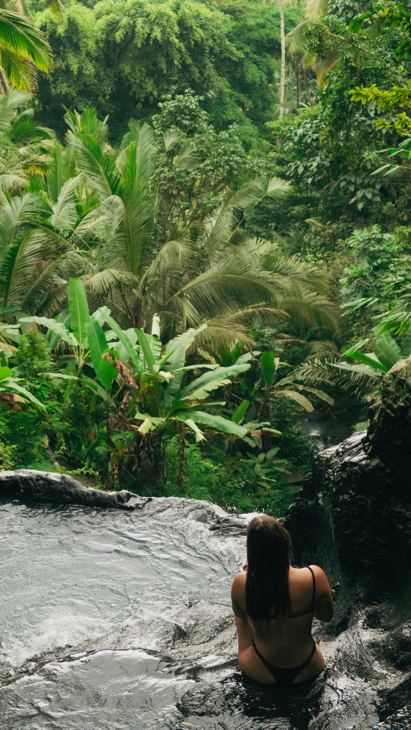 Boyana Vancheva sitting in a natural rock pool looking out over dense Balinese jungle and palms