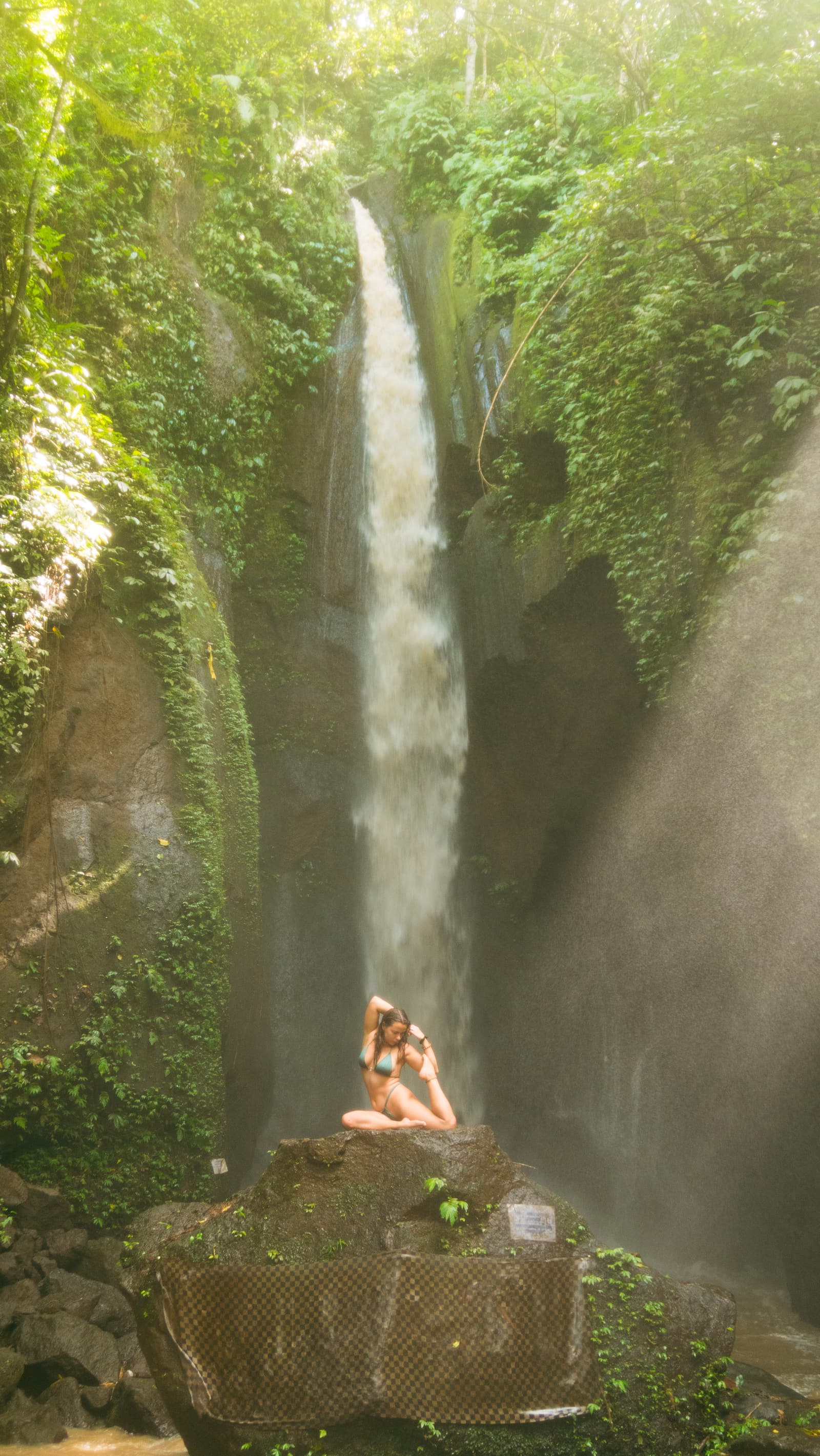 Boyana Vancheva practising a seated backbend on a rock in front of a Balinese jungle waterfall