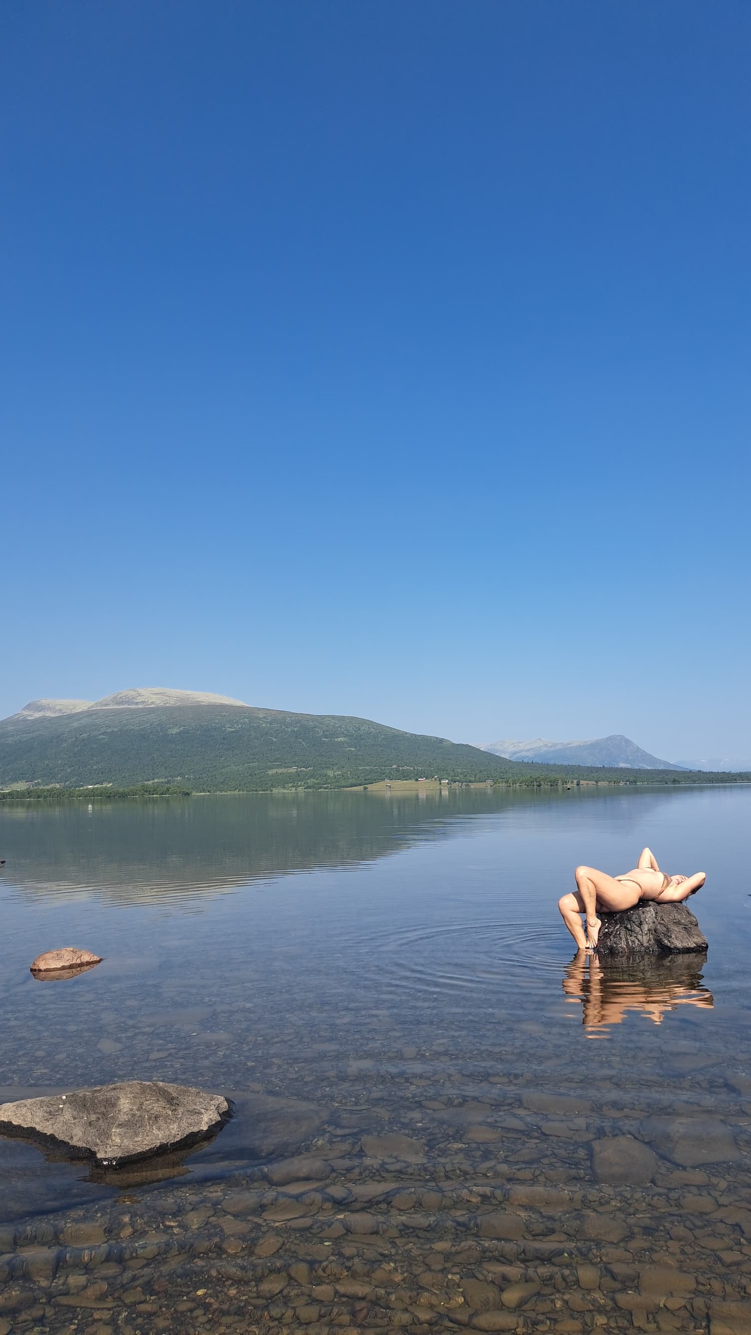 Boyana Vancheva in a supported backbend on a rock in a glassy Norwegian mountain lake
