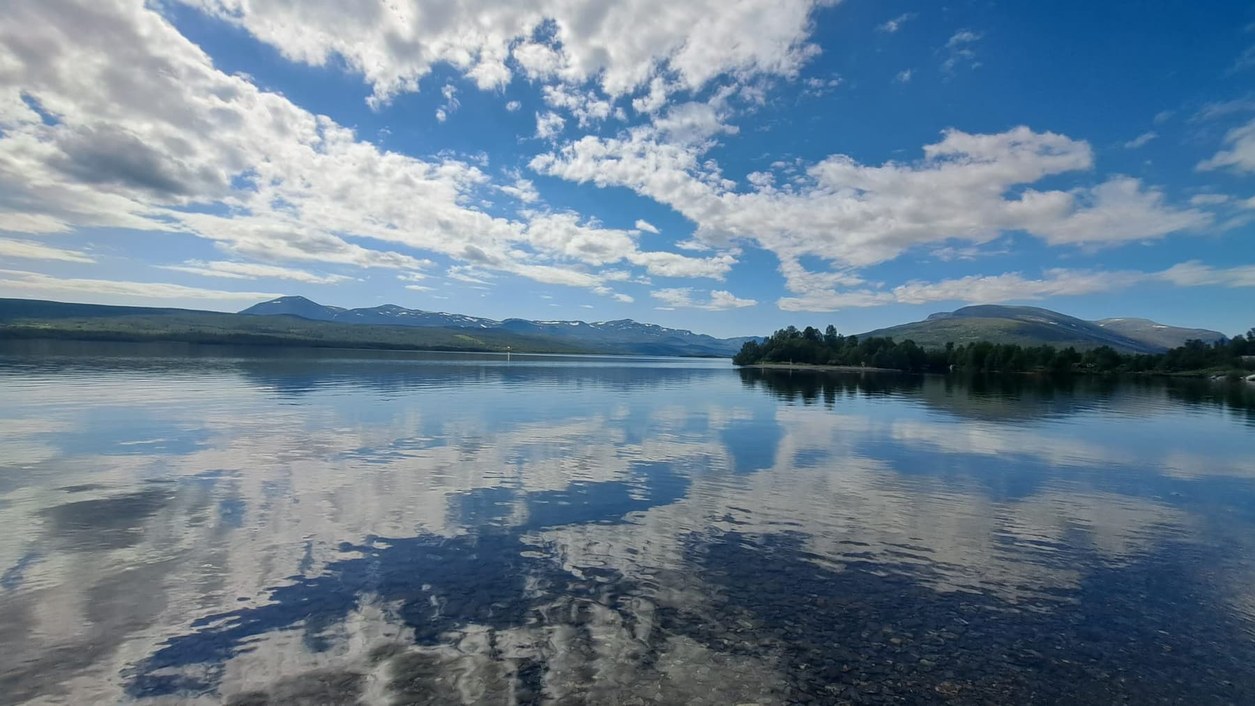 Wide still lake mirroring clouds and mountains near Nosen in Norway