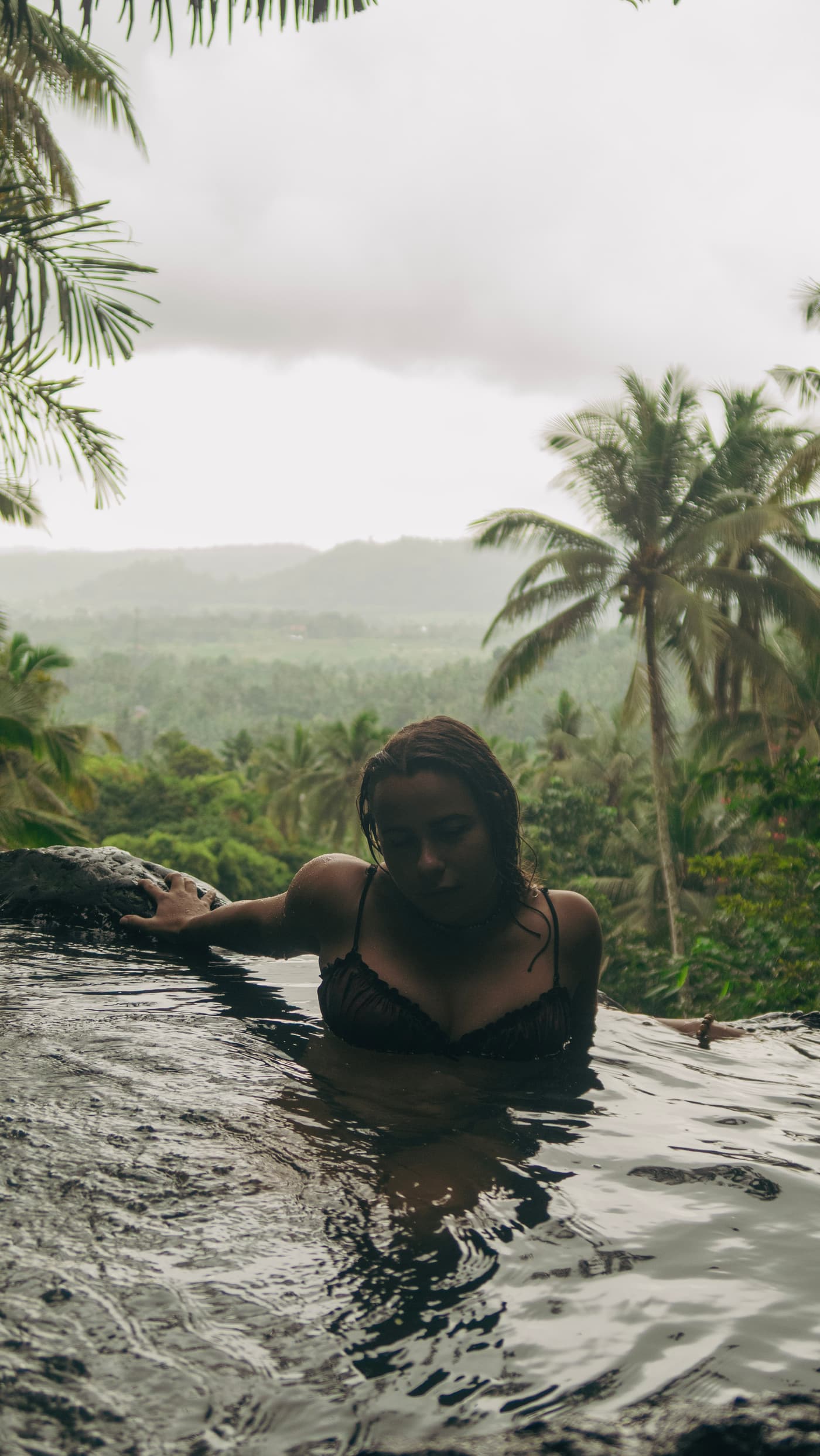 Boyana Vancheva resting in an infinity pool as rain falls over the Balinese jungle and palm trees