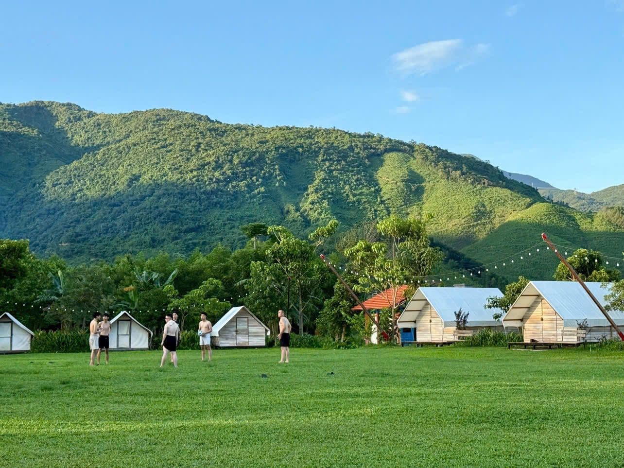 Retreat cabins on a green meadow beneath forested mountains in northern Thailand