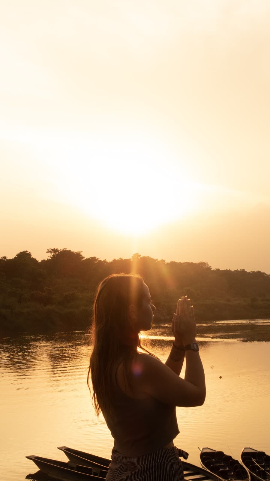 Boyana Vancheva in anjali mudra silhouetted against a golden sunrise over a Nepalese river lined with wooden boats