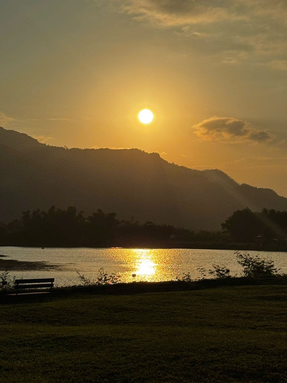 Sun setting behind a mountain ridge over a calm lake at a riverside retreat