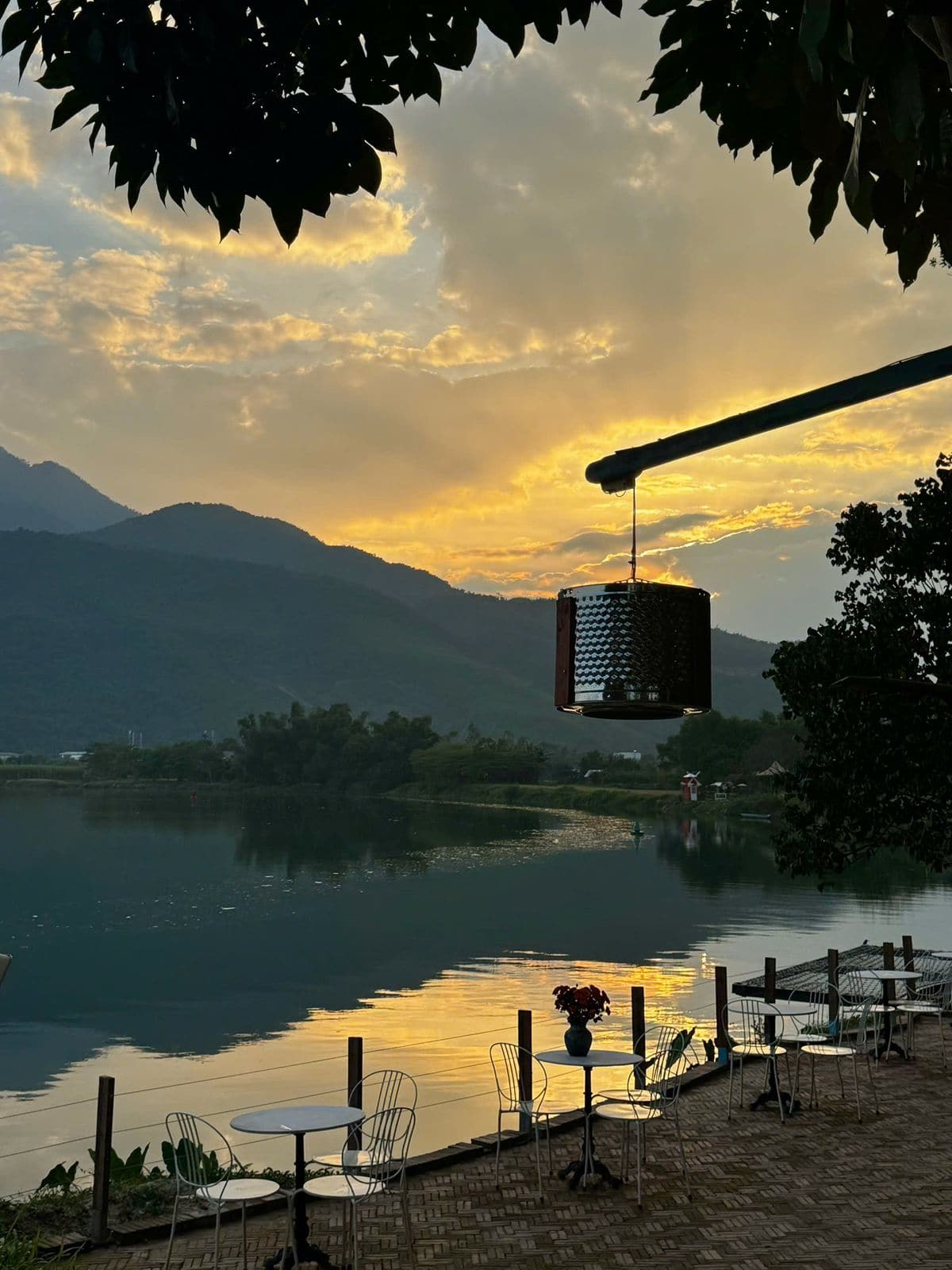 Hanging lantern silhouetted against a golden sunset over a river and mountains